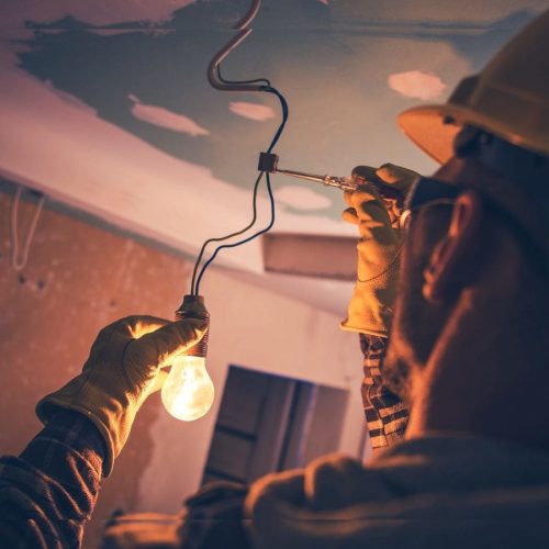 Man with safety glasses, hardhat, and gloves repairing an electrical wire